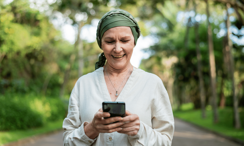 eine Frau mit einem Schal auf dem Kopf, die lächelnd auf ihr Handy-Display schaut
