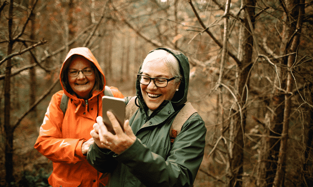 Deux femmes âgées marchant dans la forêt regardent un smartphone et sourient