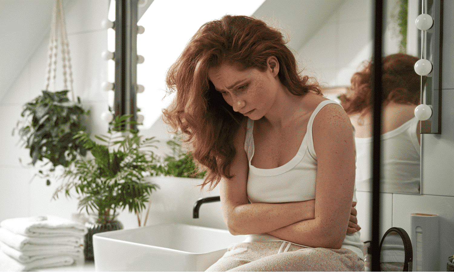 a young woman sitting next to a sink holding her stomach